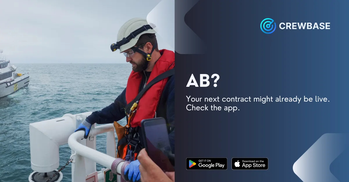 Able seaman in hard hat and life jacket on ship deck checking phone with CrewBase ad