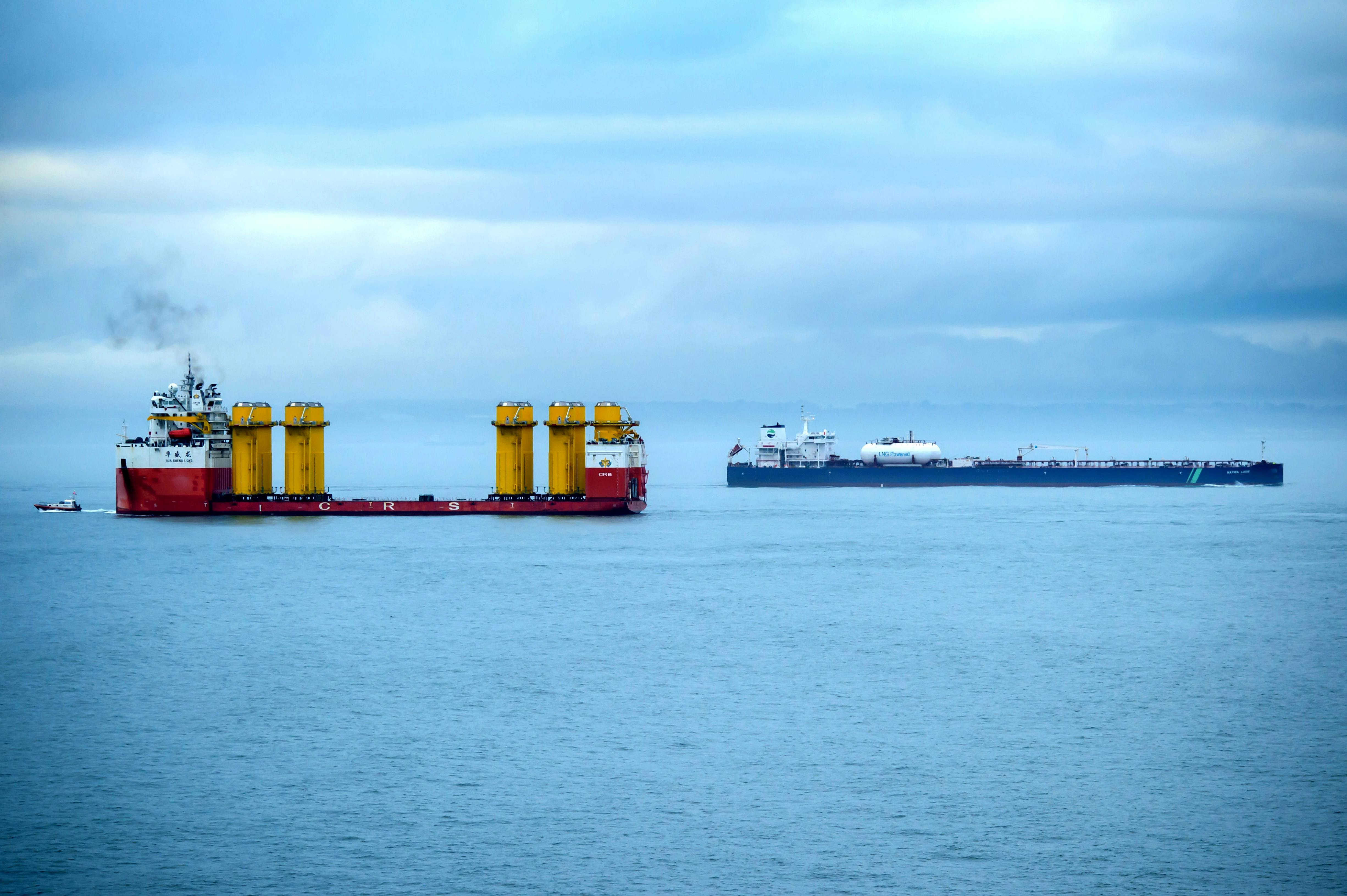 Heavy-lift vessel transporting offshore wind turbine foundations alongside an LNG-powered tanker